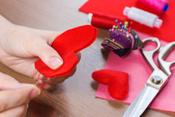 close up  view of hands sewing heart pattern cut from red fabric. sewing tools