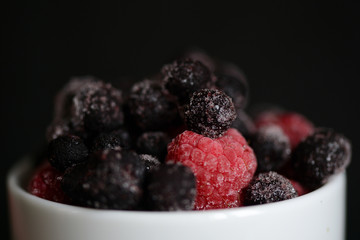 Frozen raspberries and blueberries on a dark background close up