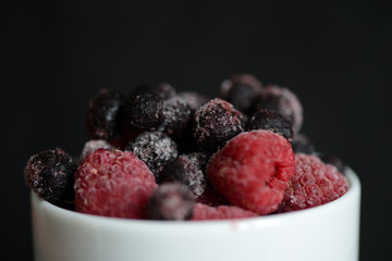 Frozen raspberries and blueberries on a dark background close up