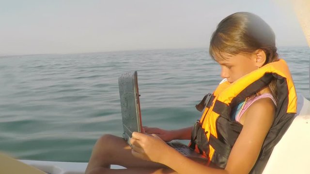 Child with laptop in the sea. Little girl in a boat in a life vest with a laptop.