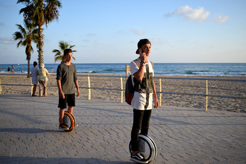 Boys are enjoying riding Monowheels scooters talking on the mobile phone on a beach promenade © Olga