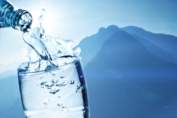 Fresh drinking water is poured in a glass against the background of mountains