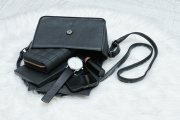 Open black bag with dropped things, notebook, mobile phone, watch and purse. Fur on background. Fashion concept