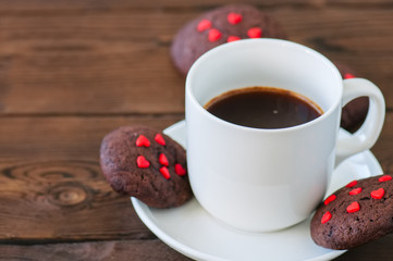 A cup of black coffee and chocolate cookies on a wooden backdrop. Valentine's Day background. Copy space.