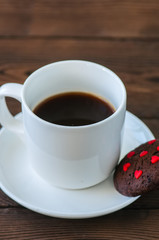 A cup of black coffee and chocolate cookies on a wooden backdrop. Valentine's Day background. Copy space.