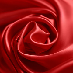 Close up of ripplesin shape of rose flower in red silk fabric. Satin textile background.