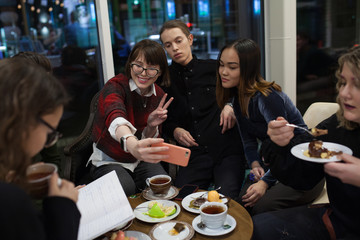 Group of positive teenagers make selfies and spending time in a cafe.