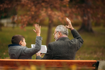 Grandpa and his grandson spend time together in the park. They are sitting on the bench. Walking in...