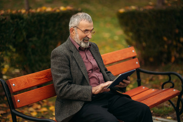 Grandpa use a tablet sitting in the pakr on the bench