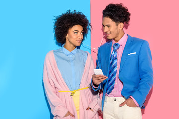 Young couple listening to music on smartphone on pink and blue background