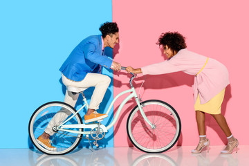 Obraz premium Happy couple having fun with bicycle on pink and blue background