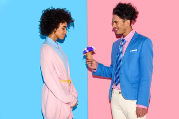 handsome man presenting flowers to attractive african woman on pink and blue background
