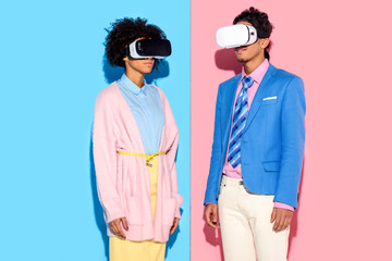 Fototapeta premium portrait of african american couple in vr headsets against pink and blue wall background