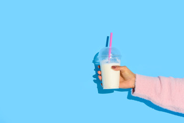 partial view of african american woman holding glass of milk with straw against blue background