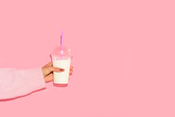 partial view of african american woman holding glass of milk with straw against pink wall