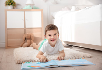 Cute little boy reading book on floor at home