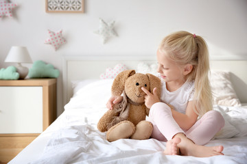Cute little girl hugging toy bunny on bed at home