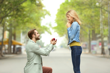 Young man with engagement ring making proposal to his beloved girlfriend outdoors - obrazy, fototapety, plakaty