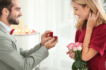 Young man with engagement ring making proposal to his beloved girlfriend in restaurant