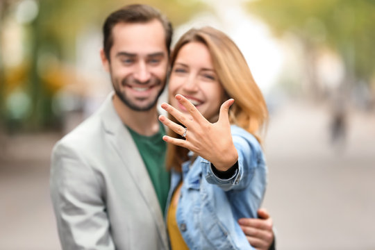 Young man with his beloved showing engagement ring outdoors
