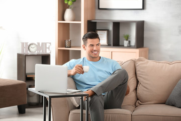 Handsome man drinking coffee while resting on sofa at home