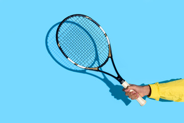 Close-up view of male hand holding tennis racket on blue background