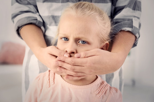 Woman covering little girl's mouth indoors. Child abuse concept