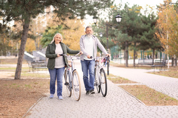 Senior couple walking with bicycles in park