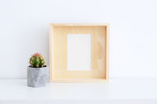 Empty wooden frame and cactus on table near white wall