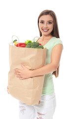 Young woman holding paper bag with groceries on white background