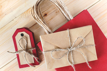 Recycled craft paper envelope, red paper bag and tags on vintage wooden table background. Top view....