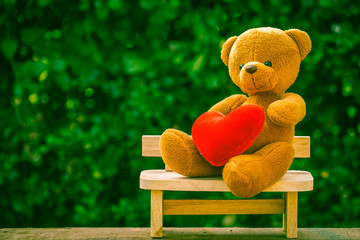 bear doll and red heart on wooden bench with dramatic tone
