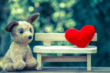 dog doll looking red heart on wooden bench with dramatic tone