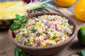 Pineapple salsa with fruit and mint in a ceramic bowl on the table