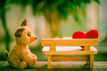 dog doll looking red heart on wooden bench with dramatic tone