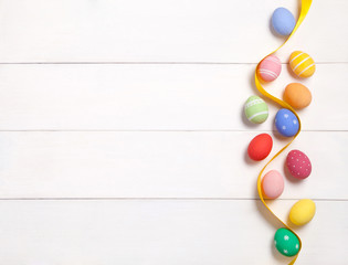 Easter composition with colored painted eggs and yellow ribbon on wooden white background with copy space. Flat lay.