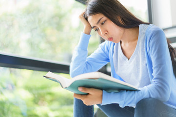 Asian young woman reading book and thinking sitting on stairs at home. concept of education, high school, university, learning and people.