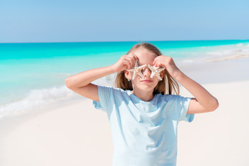 Adorable little girl with starfish on white empty beach