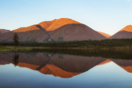 The light of the low sun on the top of the mountain. The reflection of the mountains in the lake. Yakutia.