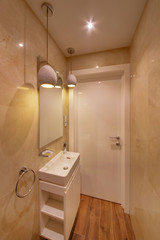 A bathroom with light walls, a white sink and a curbstone, with light lamps