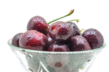 Glass vase with fresh wet cherries isolated on white background.