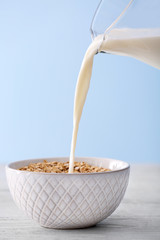 Milk pouring into bowl with oatmeal flakes on light background
