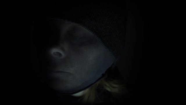 Portrait of a female criminal with black knit hat and black tights over her head lurking in the dark