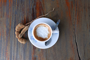 Cappuccino coffee in the white cup with coffee spoon and tamarind on the wooden table.