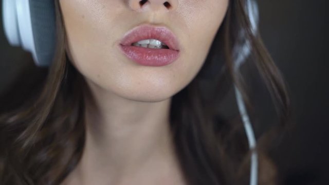 Face of sexy brunette close-up. A young woman in big white headphones is flirting with the camera. eroticly opens his mouth. chubby female lips. 4k