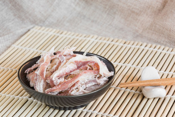 dried shredded squid in a ceramic dish on bamboo mat with copy space, delicious snack.