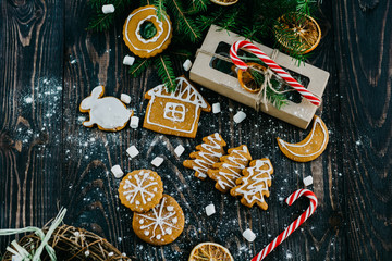 gingerbread, gift box, candy canes, fir branches and orange slices on a dark wooden background