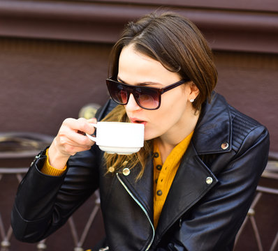 Girl in sunglasses drinks tasty coffee on brown terrace
