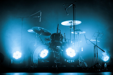 A kit of drums and a microphones on an empty stage in blue smoke before the concert