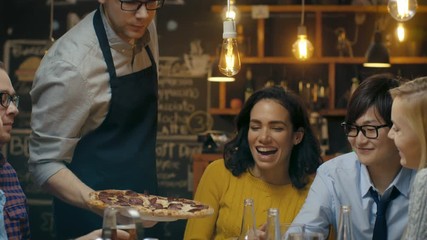 Waiter Serves Delicious Pizza to a Diverse Group Of Hungry and Happy Friends. They Eat, Drink and Have Fun in this Stylish Looking Bar. Shot on RED EPIC-W 8K Helium Cinema Camera.